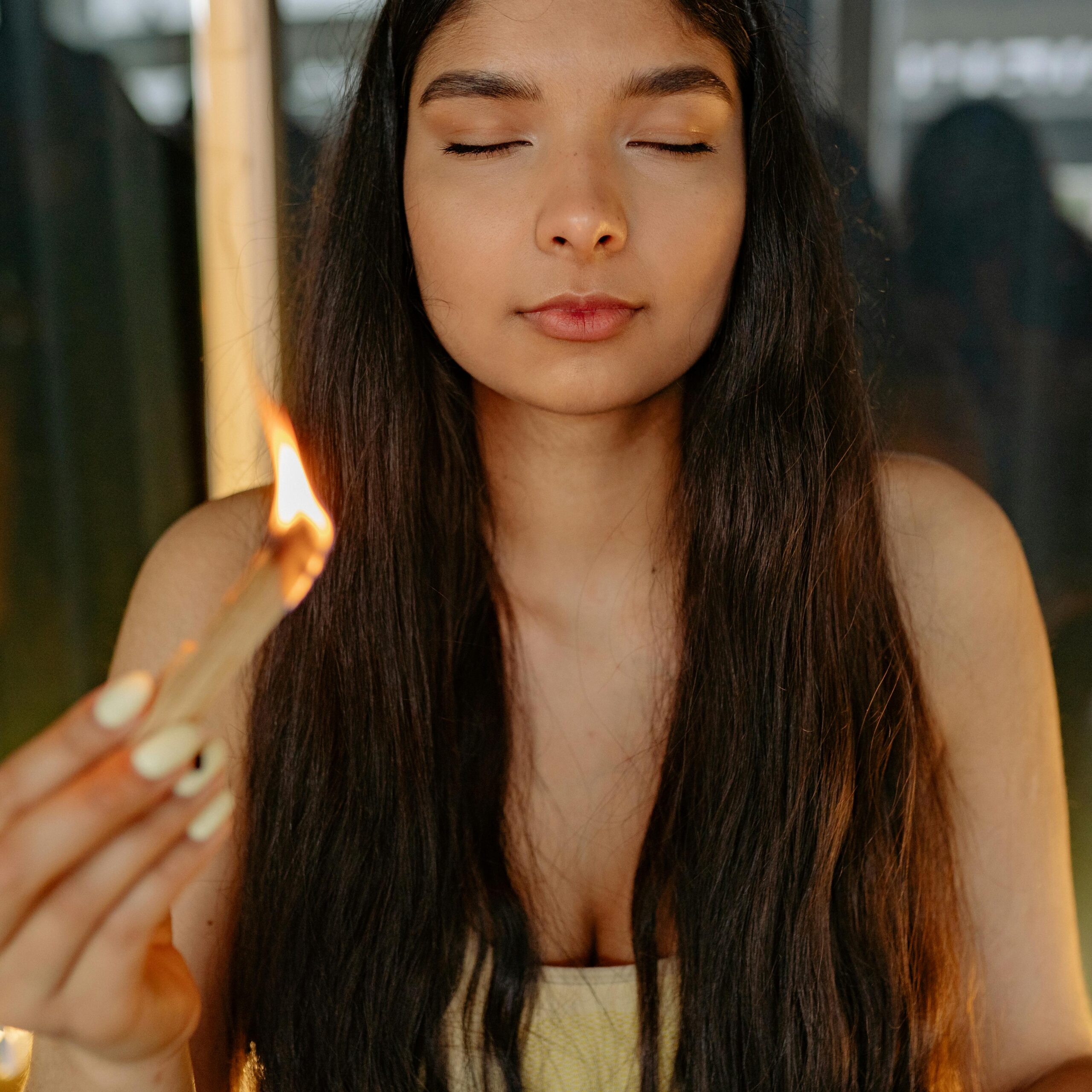 A serene woman meditating indoors, holding a burning incense stick with eyes closed, practicing mindfulness.